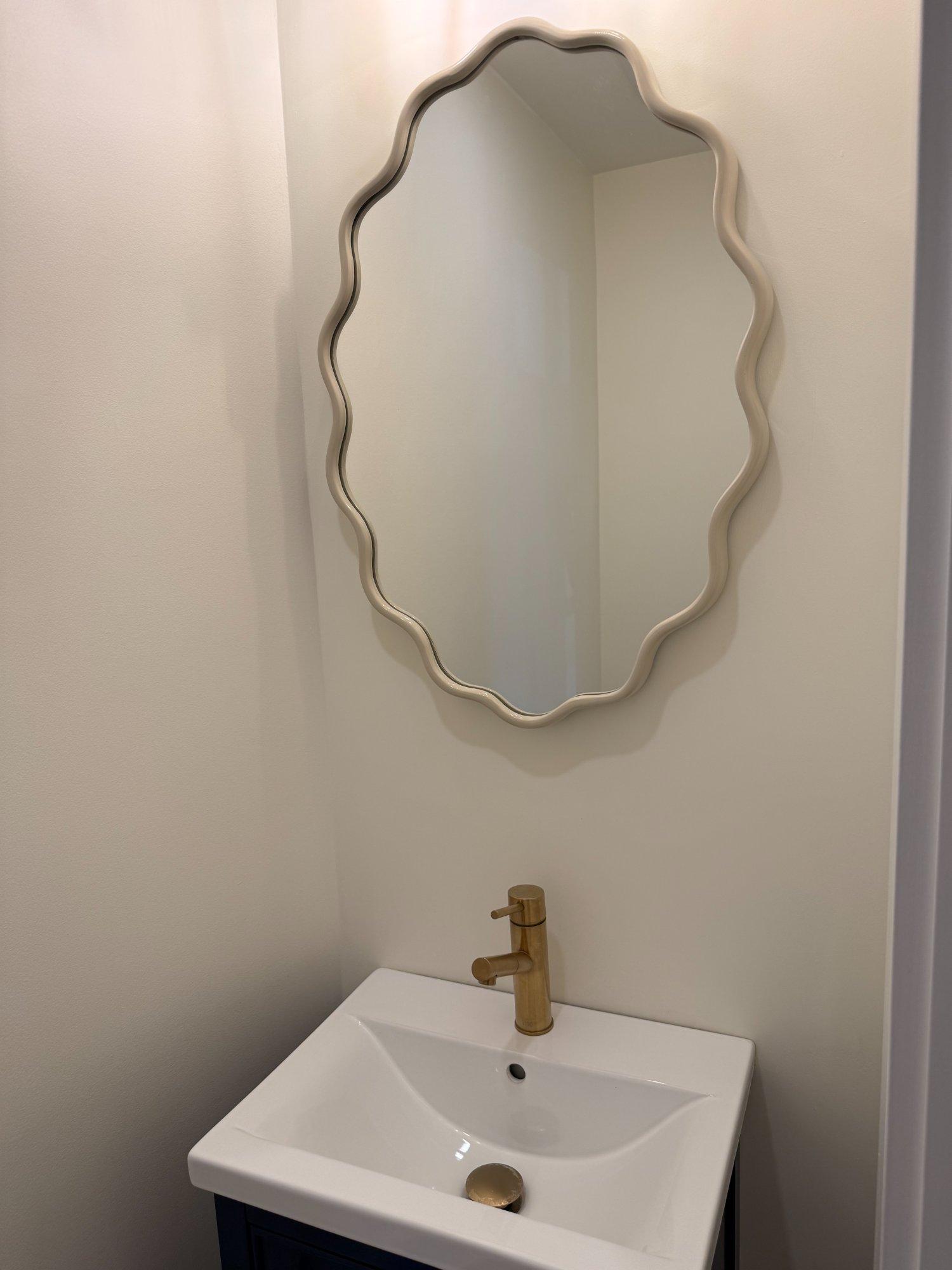 Half bath vanity with wavy decorative mirror and brushed gold faucet