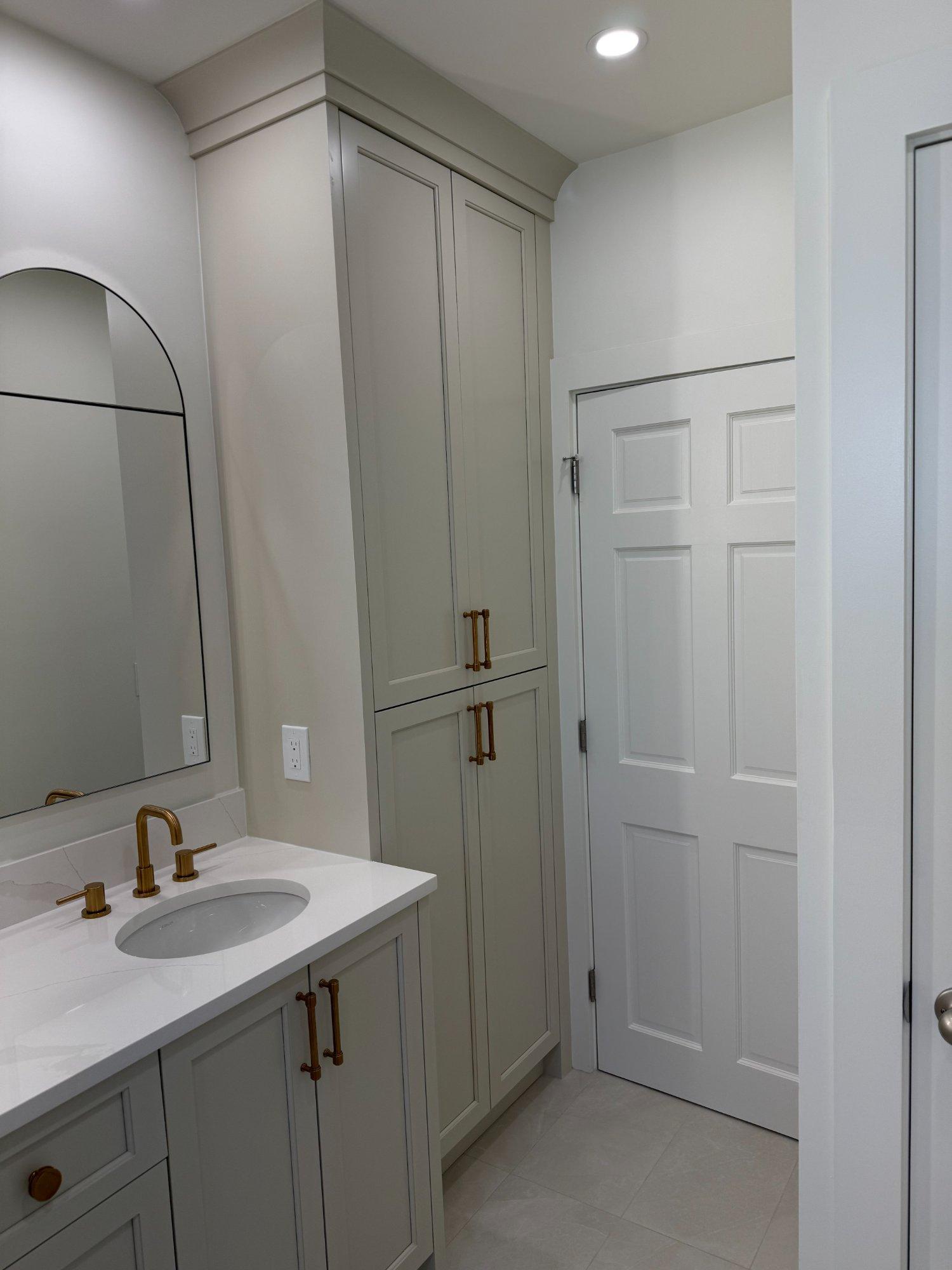 Tall linen tower cabinet with brushed gold pulls beside single sink vanity