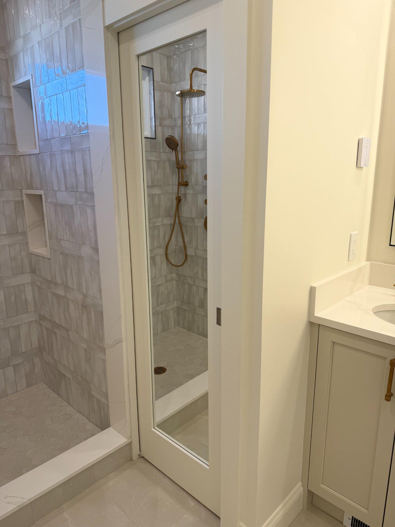 Master bath walk-in shower viewed through glass door with handmade tile and vanity