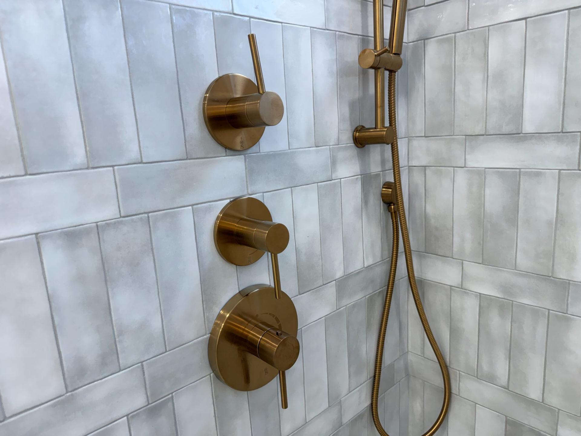 Brushed gold thermostatic shower valve and hand shower detail on handmade tile