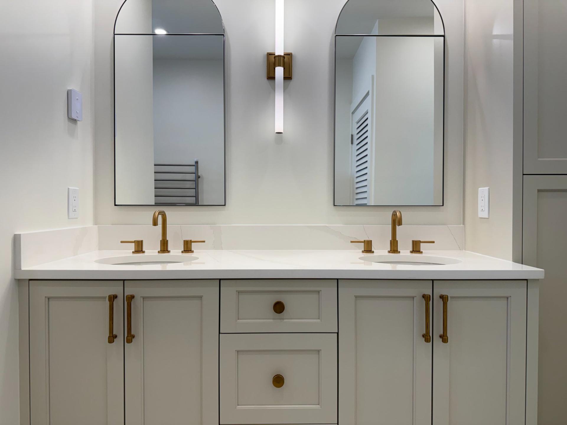 Double vanity with arched mirrors, quartz countertop and brushed gold wall sconce