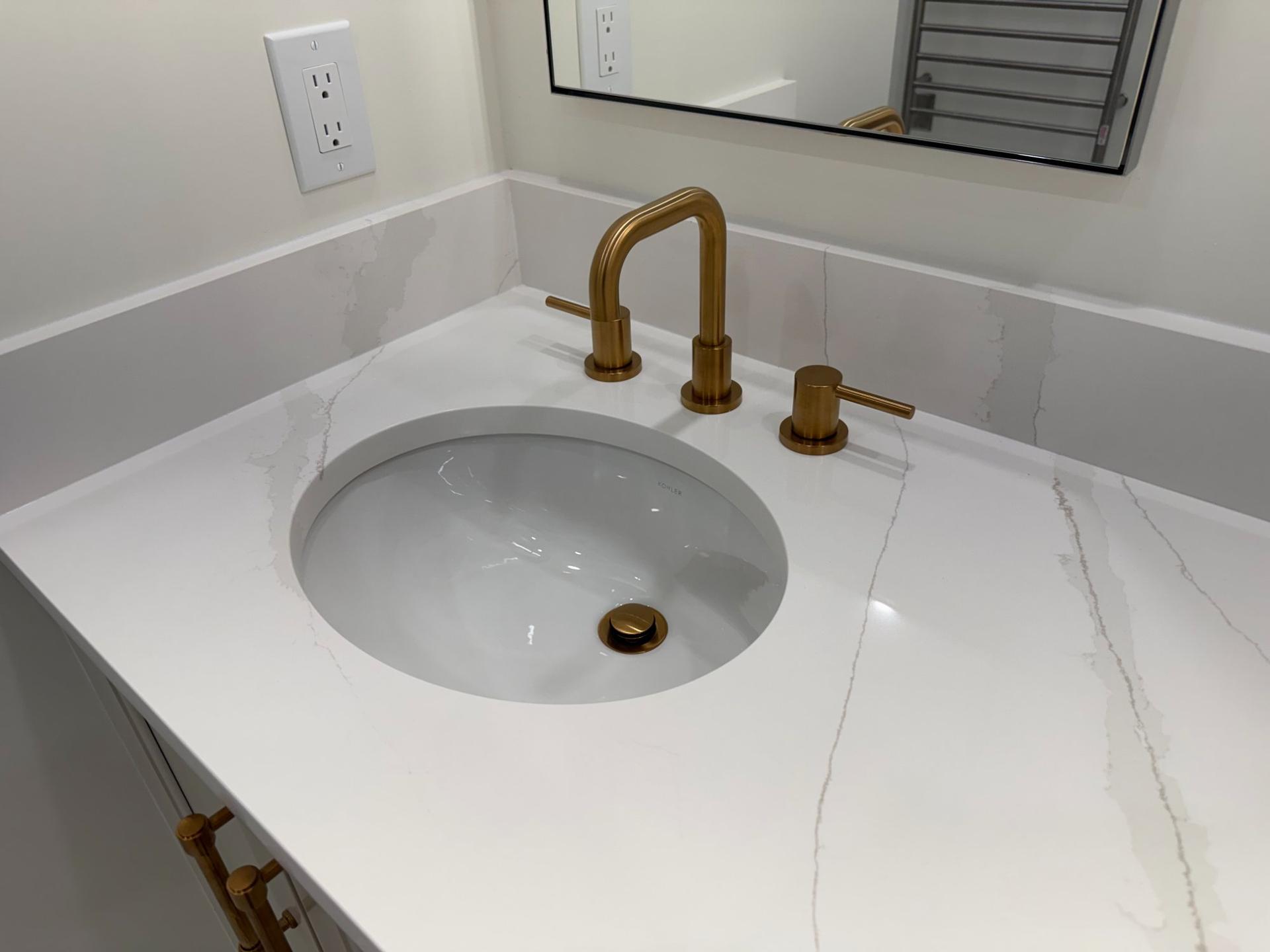 Undermount sink with quartz countertop and brushed gold widespread faucet detail